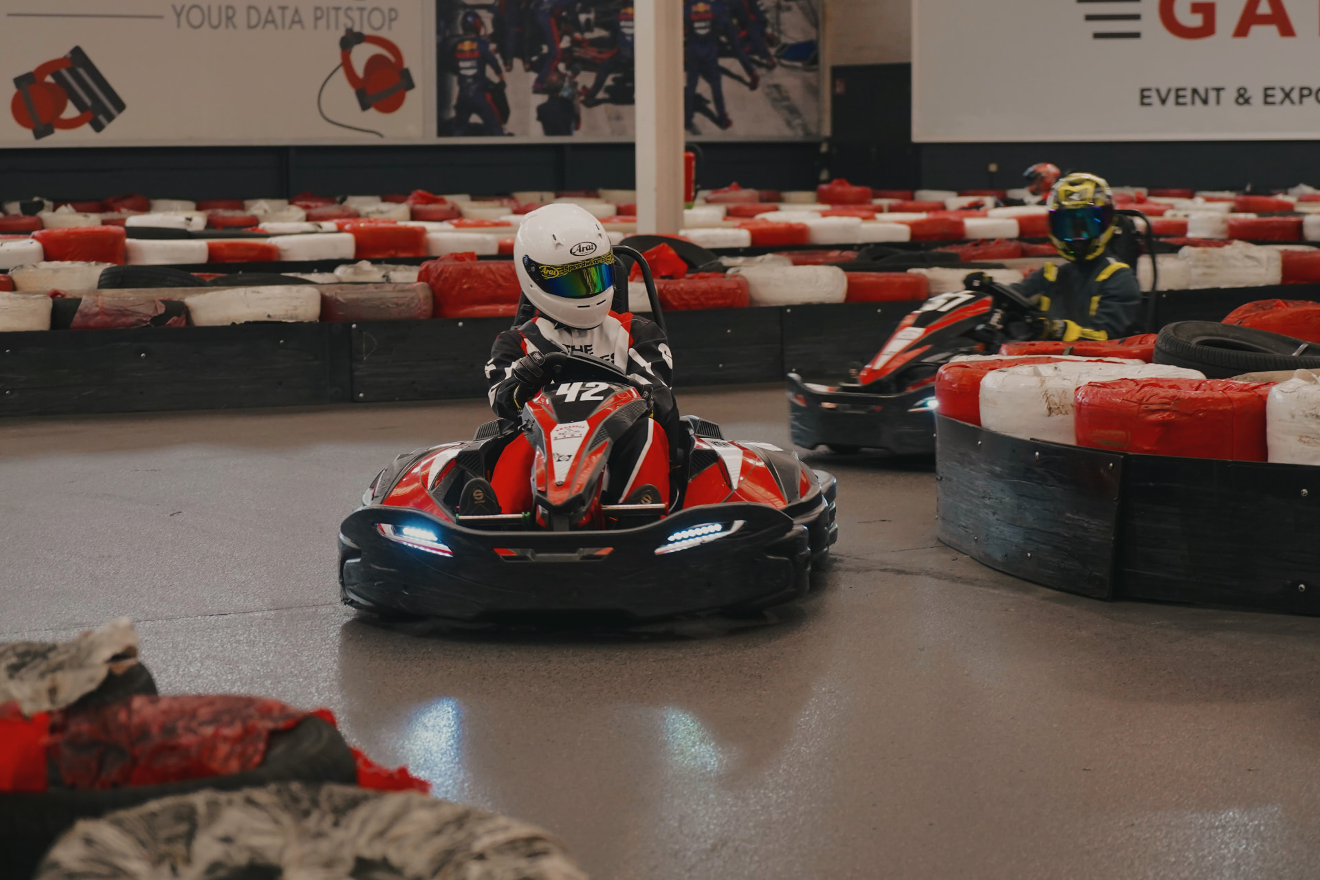 Pilote BEKC au volant du kart électrique n°42 sur une piste indoor éclairée en néon cyan